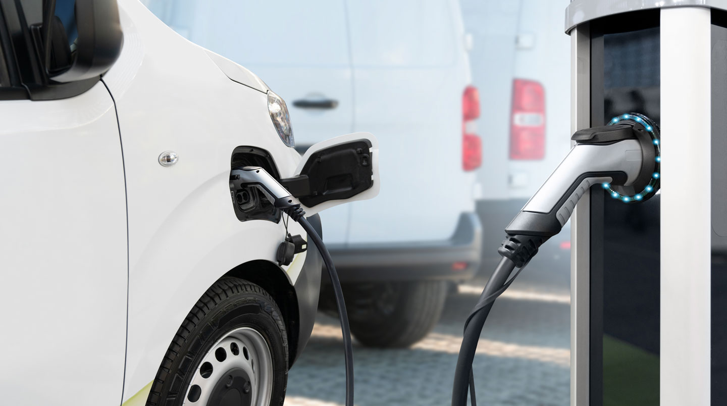 Véhicule électrique français connecté par câble à une borne de recharge rapide sur une aire d'autoroute, avec infrastructure moderne visible